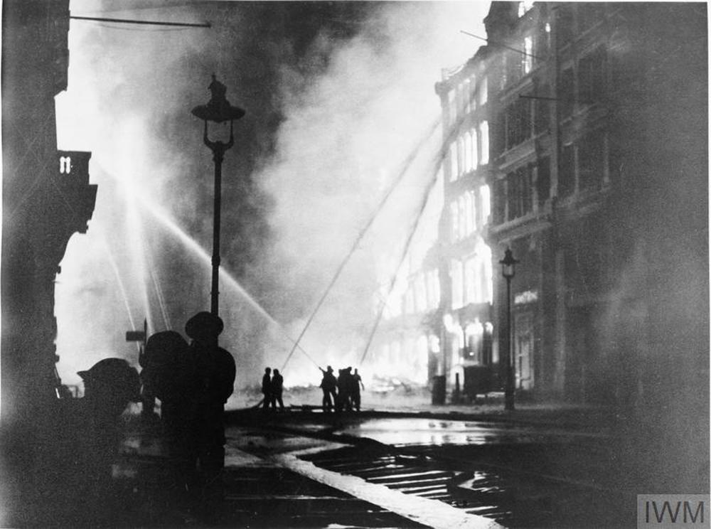 Firefighters tackling burning buildings, firing powerful jets of water from hoses, in central London during the Blitz.