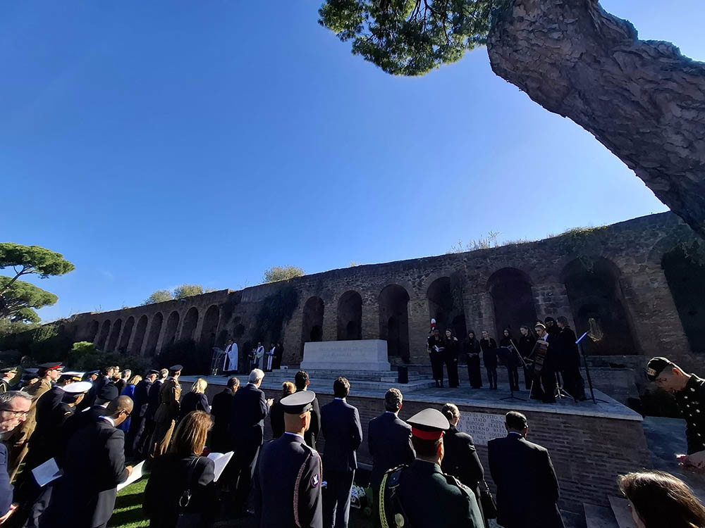 A crowd watches a choir performing on a raised platform for Remembrance Sunday in Rome War Cemetery.