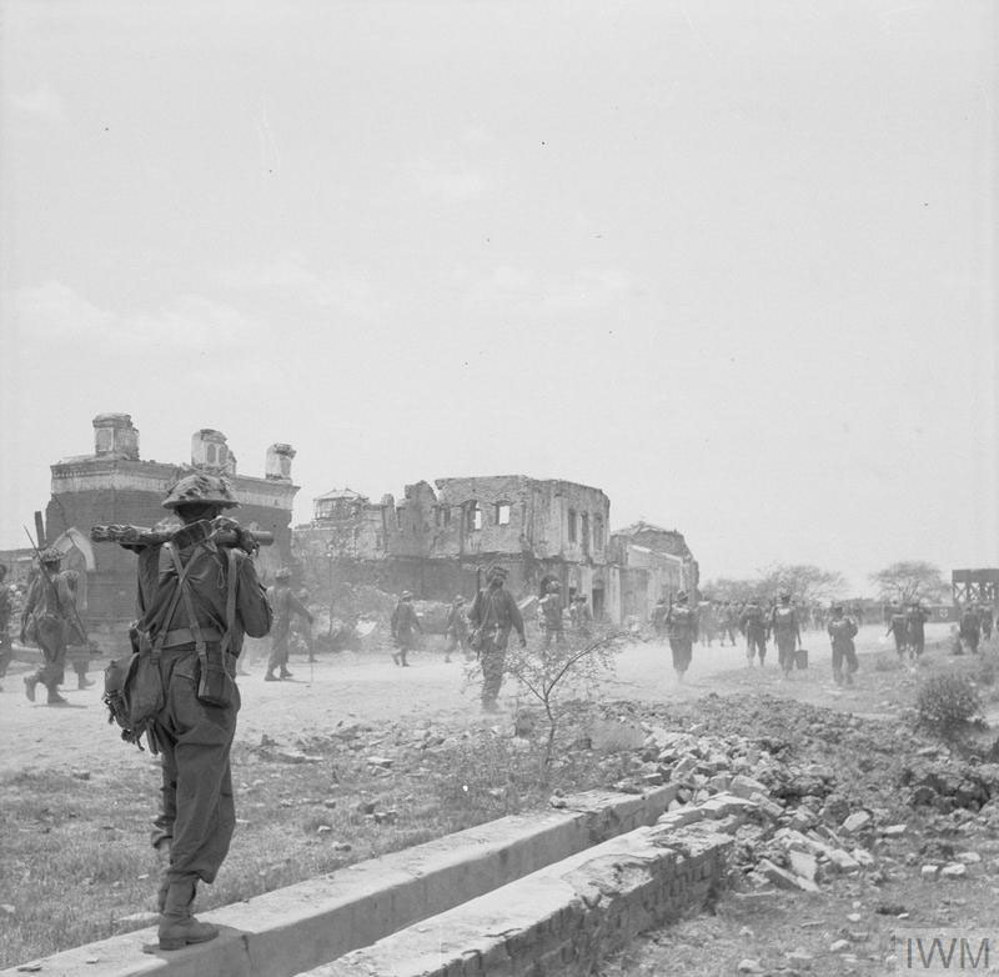 Indian Army troops move through the ruins of a smashed up Burmese town on their way to Rangoon, Spring 1945.