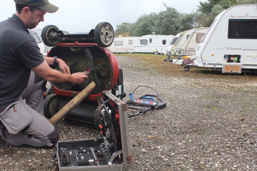 A man using an extensive tool kit to tighten bolts on the underside of a lawnmower.