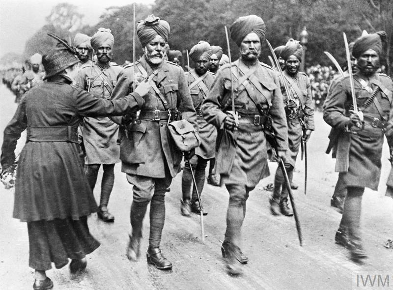 Sikh Indian Army soldiers marching down a road in France at some point during the First World War. A woman can be seen attaching a flower to the lapel of one of the marching soldiers.