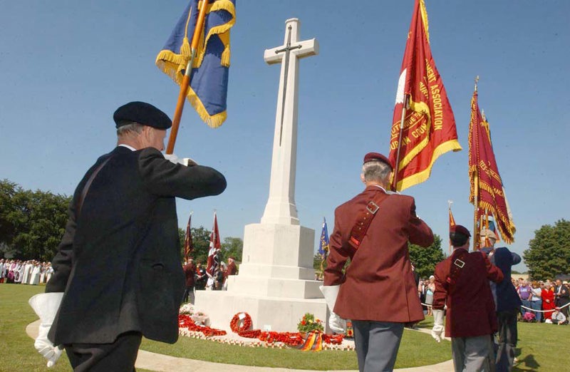 D-Day Veterans parade regimental flags around the Cross of Sacrifice at Bayeux War Cemetery.
