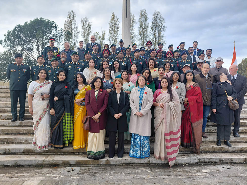 Indian Army and civilian delegation members stand on the steps of the Cross of Sacrifice at Cassino War Cemetery.