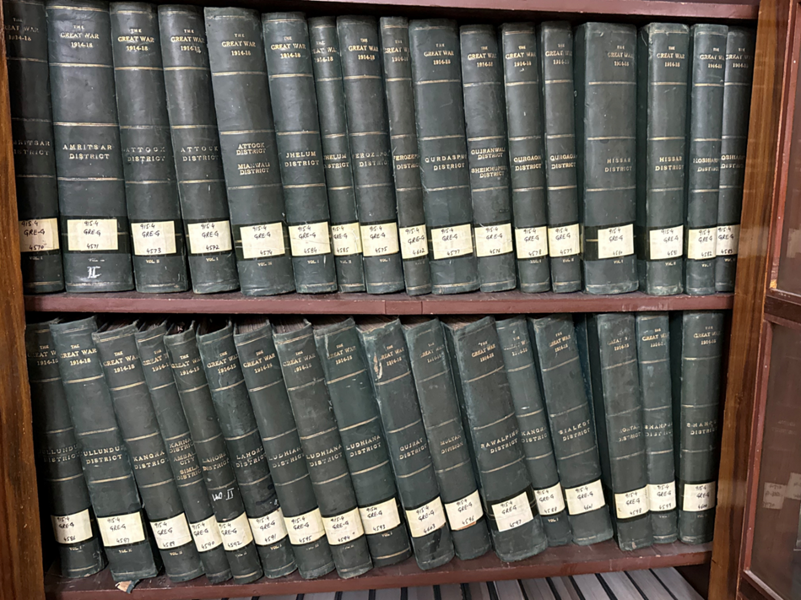 Several leather-bound volumes of the Punjab Registers on a wooden bookcase.