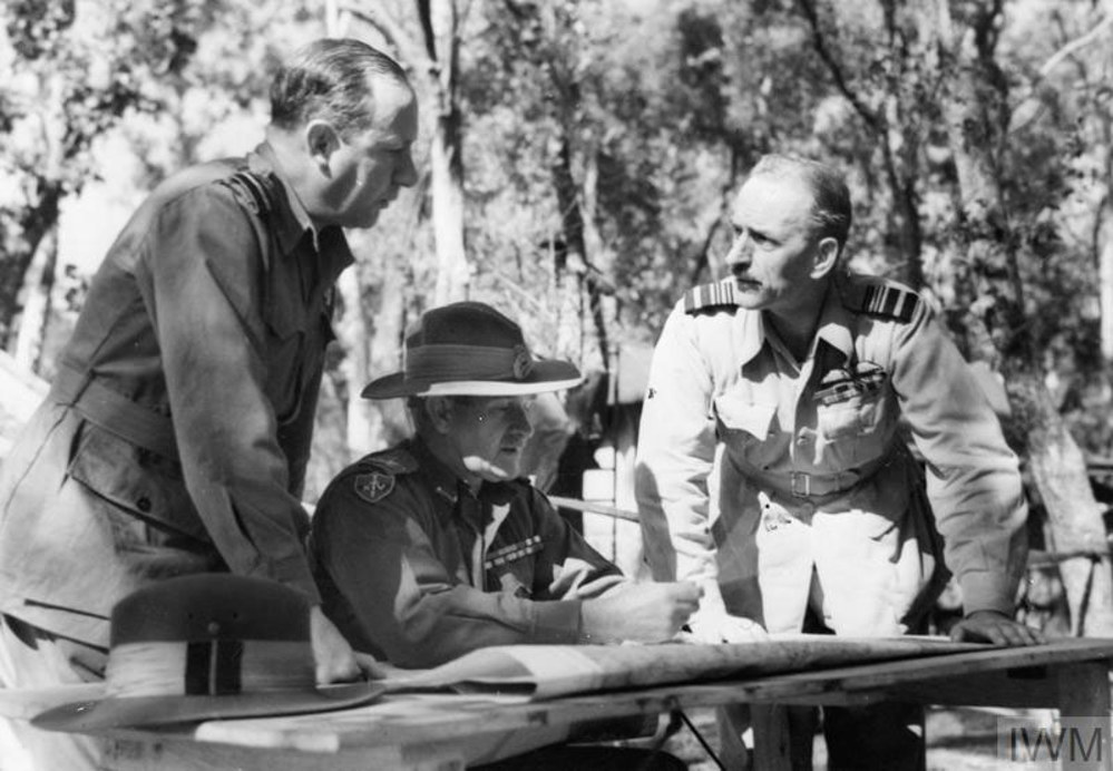 British Commanders in Burma discussing operations. General Bill Slim is sat down at a map-strewn, flanked by two army officers.