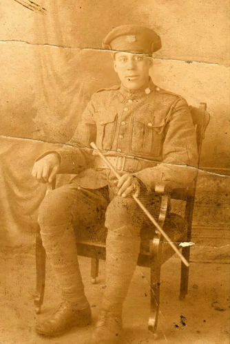 Private Charlie Some sitting on a charge in his military unifrom. He is holding a short military batton.