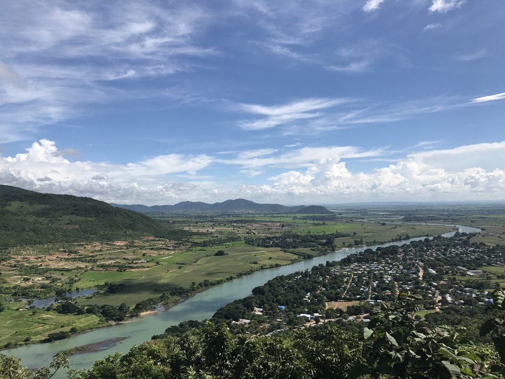 Aerial view of the Sittang River winding through the Myanmar countryside. A small town is visible on the eastern bank while hills and mountains are visible in the background.