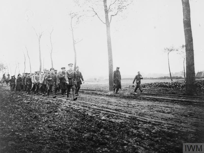 A column of German Prisoners of War being escorted into Ypres along a muddy road.