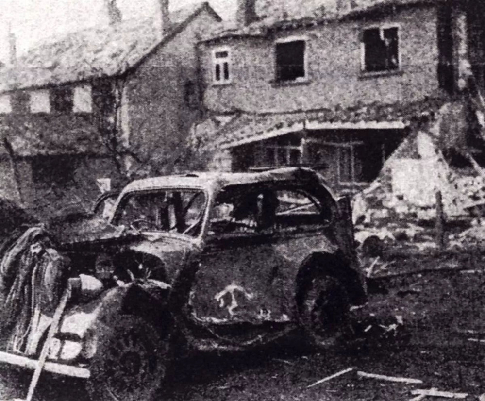 A burned out wrecked car sits in front of a badly damaged house following a V-1 Attack on Greater Manchester.