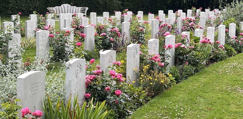 Bright flowers and blooms adorn the headstones at a CWGC cemetery, including pink roses and yellow flowers.