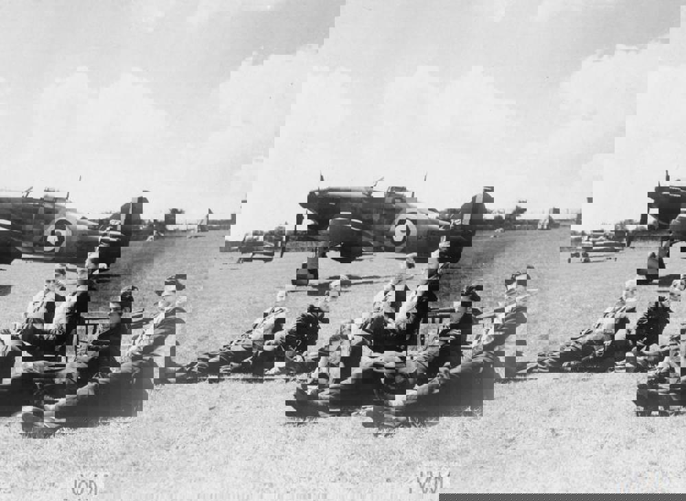 Battle of Britain Pilots sat on grass in front of their Hurricane aircraft.
