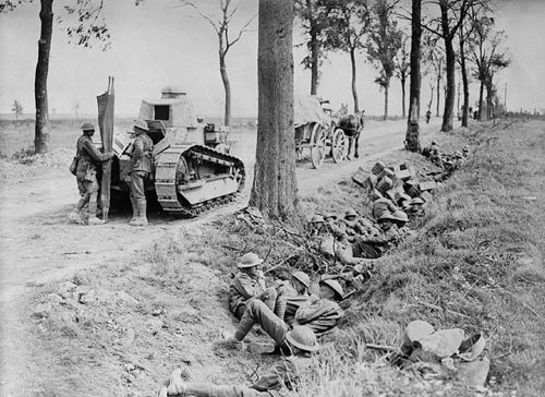 Canadian infantry shelter beside a road next to tall trees and a WW1-era light tank