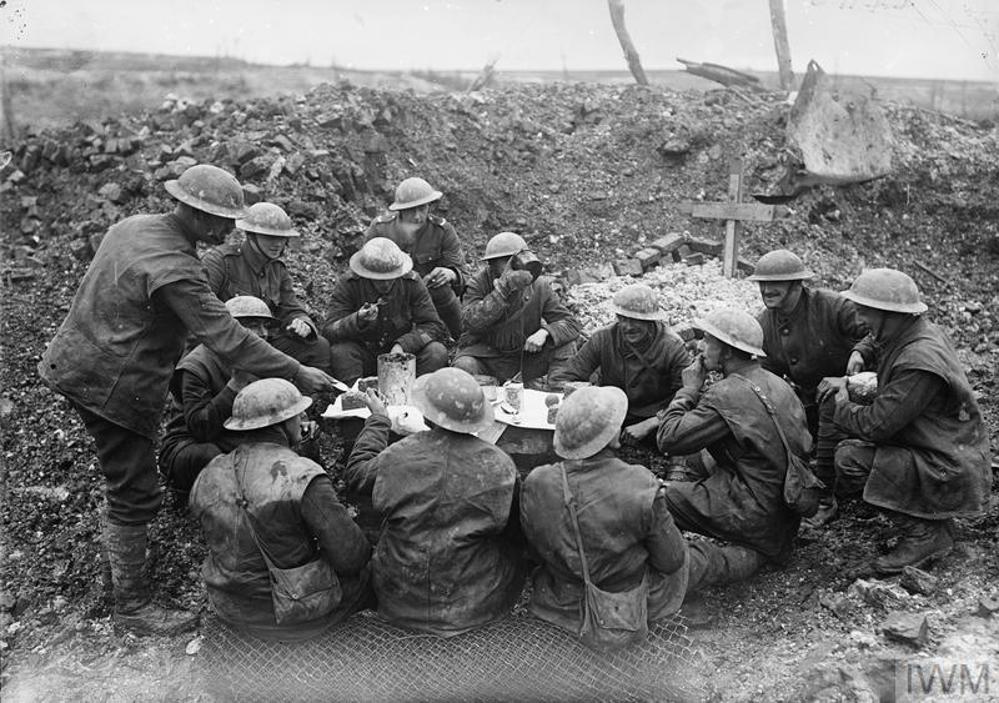 British soldiers eating Christmas dinner on a table and chairs set up in a shell crater somewhere on the Western Front during World War One.