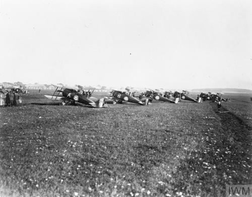 A line of First World War biplanes sit on a muddy field waiting for take off.