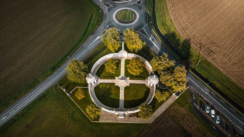 Overhead view of the Neuve-Chapelle Memorial showing its location next to the main road and roundabout near the village of Neuve-Chapelle. Farmers fields flank the memorial and the roads.