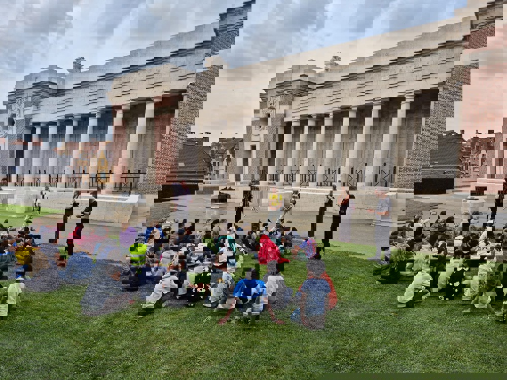 Tour guides speaking to a group of seated adolecents on the Rampart side of the Menin Gate Memorial, Ypres
