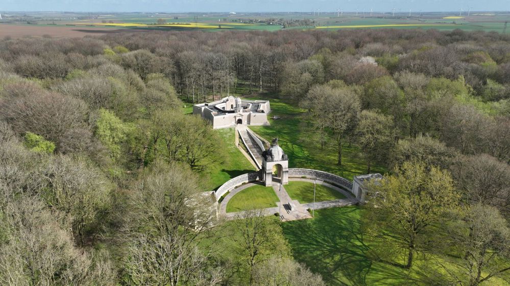 South Africa (Delville Wood) National Memorial sitting amid the wood itself. The memorial is a round curtain wall with a central tower/gateway followed by a stone path leading to a star-shaped museum building.