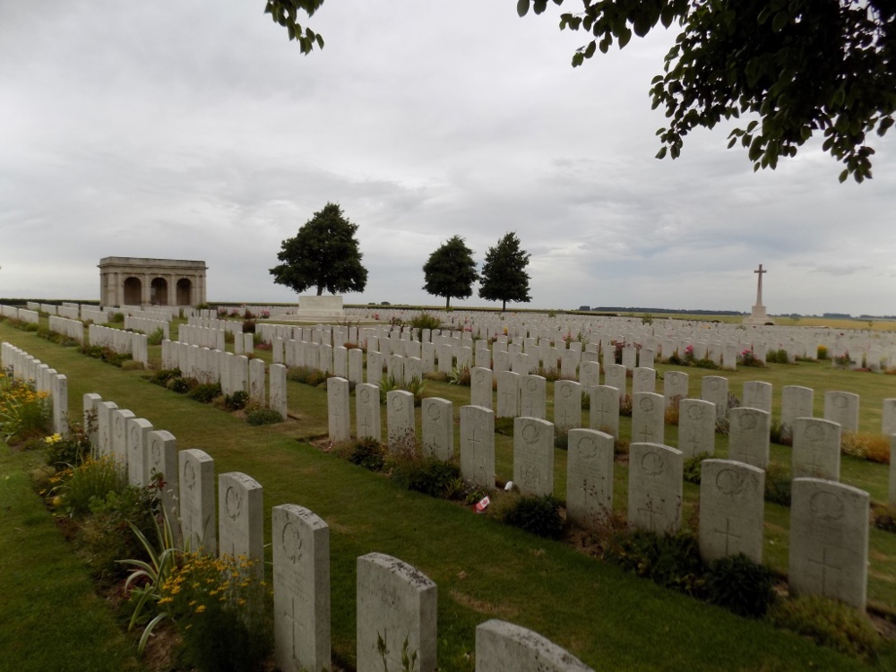 Rows of headstones with the Cross of Sacrifice in the far right of the picture and the Stone of Remembrance and columned entryway at Adanac Canadian Cemetery.
