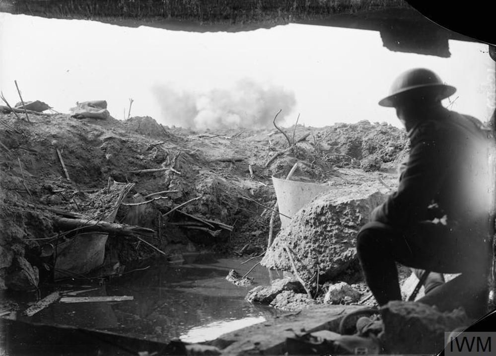 A British soldier looks at the view of No Man's Land from a captured German Pill Box at Passchendaele, circa late 1917,. The ground is a churned mess of logs, wire, and shell craters. A plume of smoke is visible on the horizon.