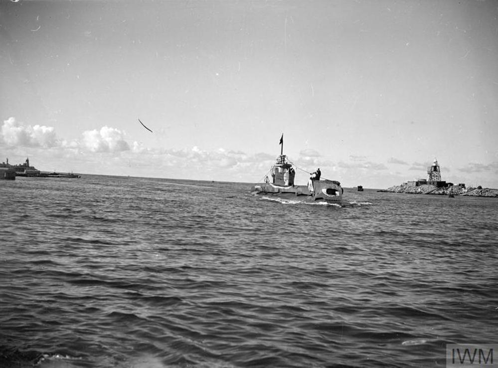 WW2-era submarine HMS Trenchant sailing on the surface as she returns to port. A  rocky outcrop with a structure built on top is visible in the background.