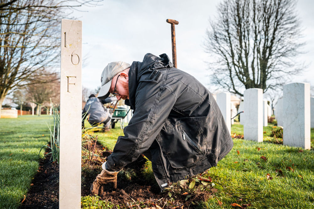 A gardener working on a plant border at Bayeux War Cemetery.