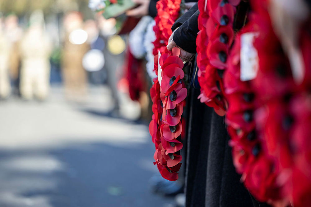 Close up of men holding red poppy wreaths at a Remembrance Day event.