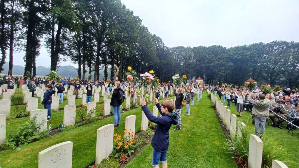 Schoolchildren and townsfolk laying colourful flowers on the war graves at Arnhem Oosterbeek War Cemetery.