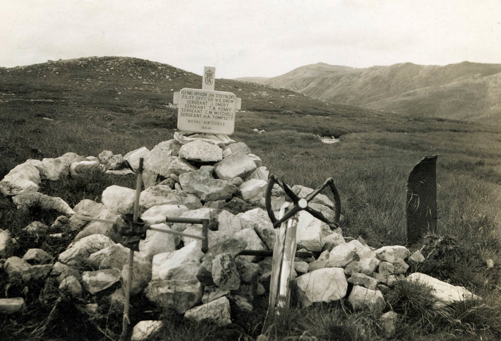 A stone marker placed on top of a rough cairn. Plane crash wreckage has been used to make imprompteu grave markers.