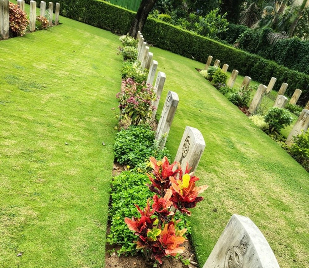 Variety of colourful plants and flora set against a bright green lawn and white limestone CWGC headstones at Ranchi war cemetery.