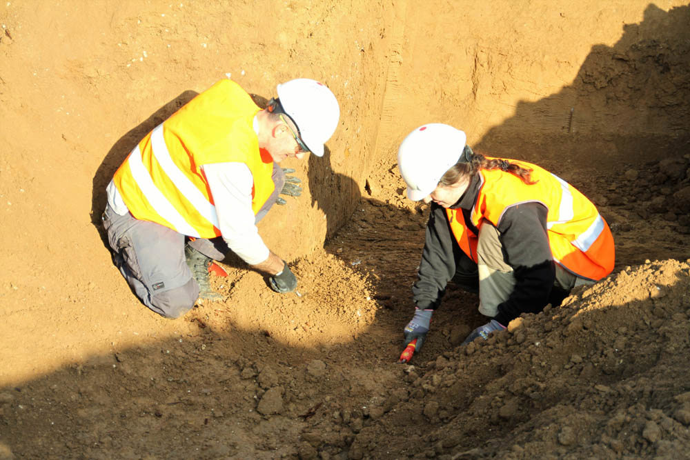Men in orange hi-vis vests and hard hats digging in a deep trench.