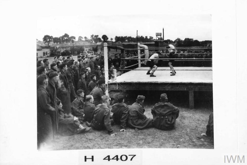 A regimental boxing match taking place in the early 1940s. British soldiers gather around a boxing ring to watch two comrades spar it out for the championship.