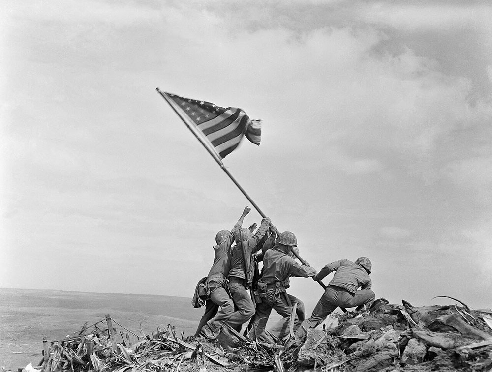 "Raising the Flag on Iwo Jima" by Joe Rosenthal showing a group of US marines raising the US flag on high ground during the Battle of Iwo Jima, WW2.