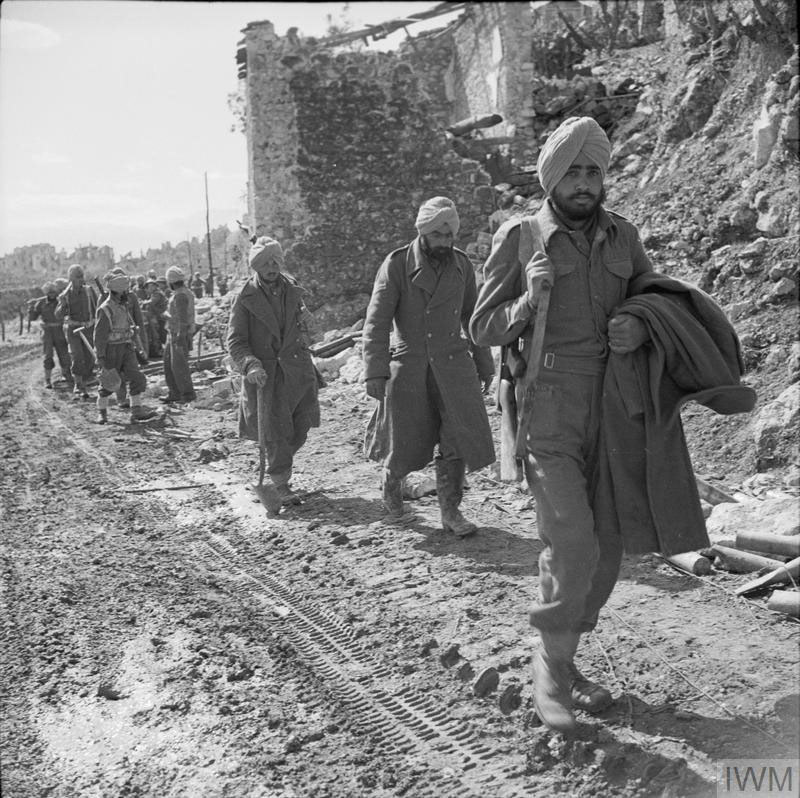 WW2 era Sikh soldiers moving through rubble along a dirt road at the Battle of Monte Cassino