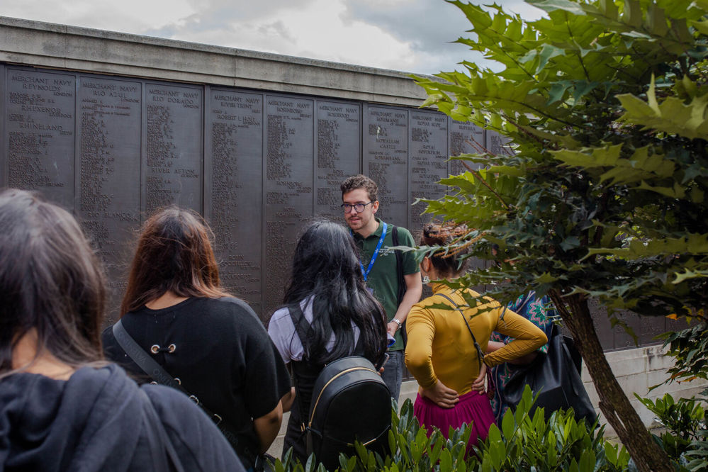 A CWGC Public Engagement Coordinator showing tour guests around the Tower Hill Memorial with the bronze memorial name panels in clear views.