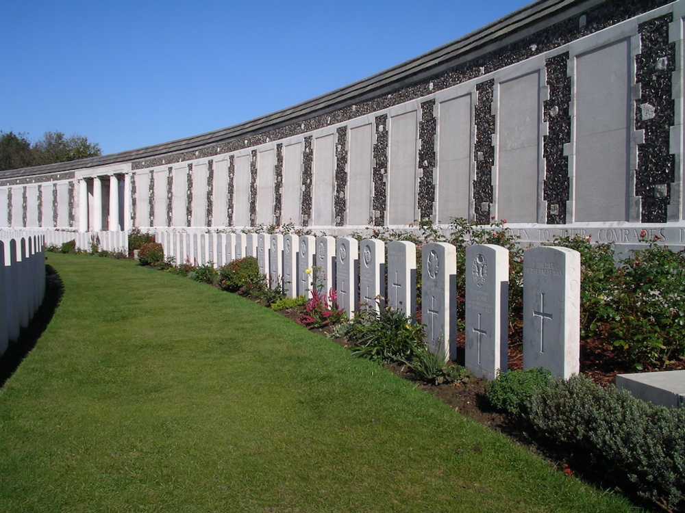 Row of headstones and bushes in front of the Tyne Cot Memorial
