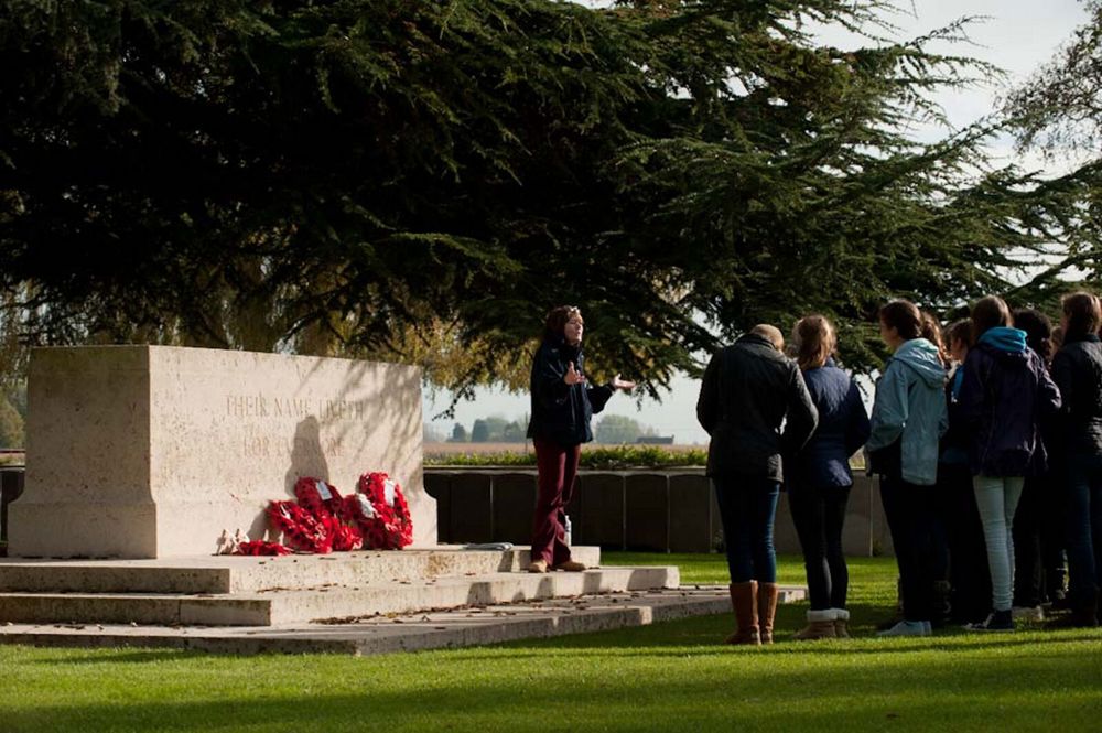 Tour Guide talking to guests on the steps of the Cross of Sacrifice and Lijssenthoek Military Cemetery.