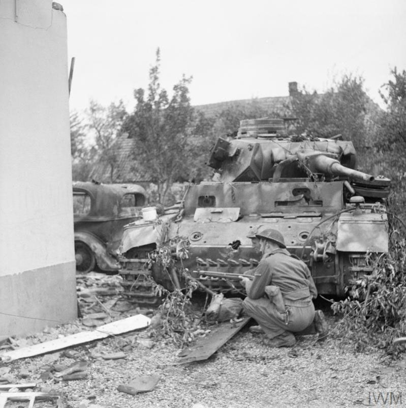 A british soldier kneels behind a destroyed German tank at the Battle of Arnhem