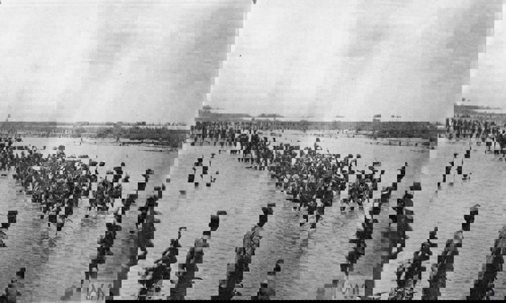 Soldiers, porters, and carriers of the King's African Rifles wading through a low river.