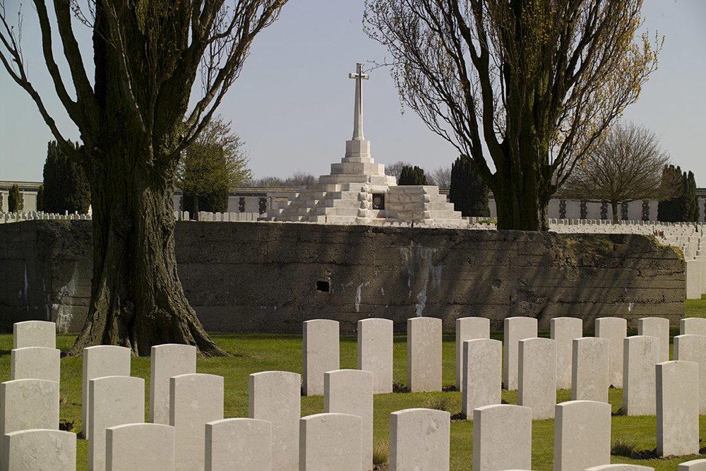 View of Tyne Cot Cemetery with the remains of a German WW1 bunkhouse set behind headstone rows and in front of the Cross of Sacrifice.