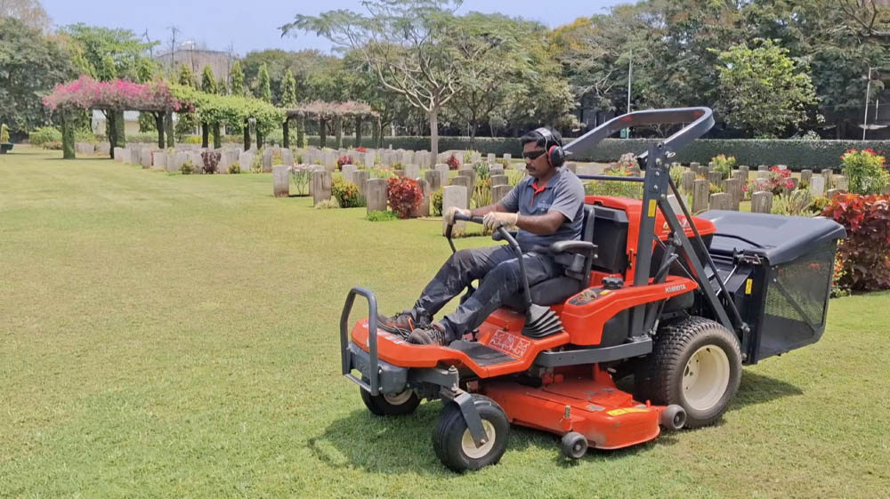 A CWGC gardener sits atop a large red ride on lawnmower.