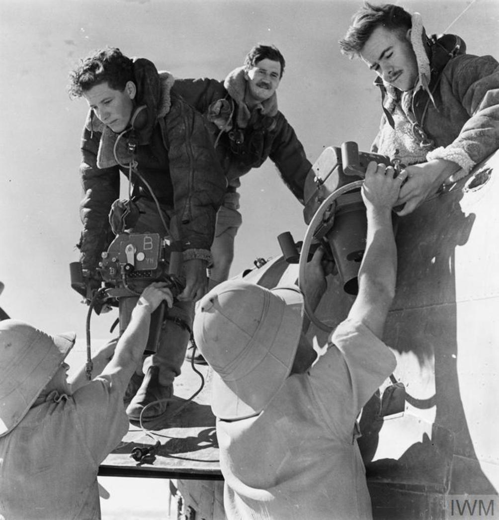 WW2 era recon pilots being handed big chunky film cameras from ground crew in the process of loading them into an aircraft.